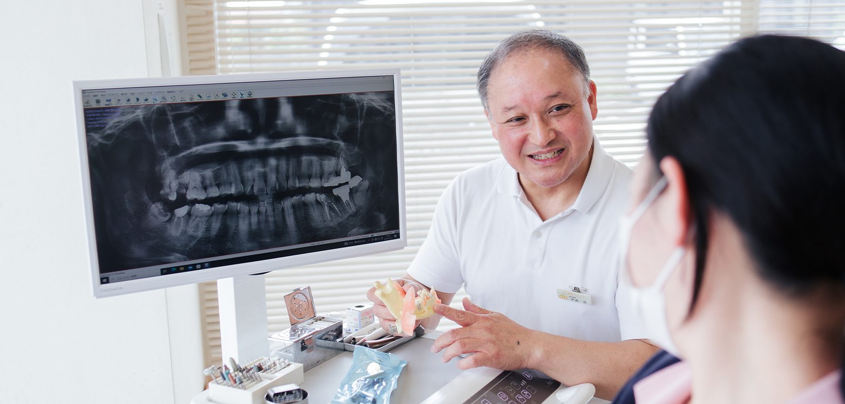 レントゲン画像と模型を使いながら、笑顔で患者さんに説明する院長